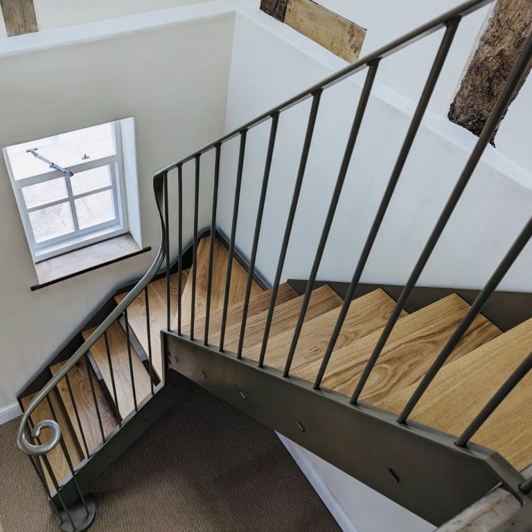 Wrought iron staircase featuring wooden tread, a quarter turn at the window level and a swirling finish at the newal.